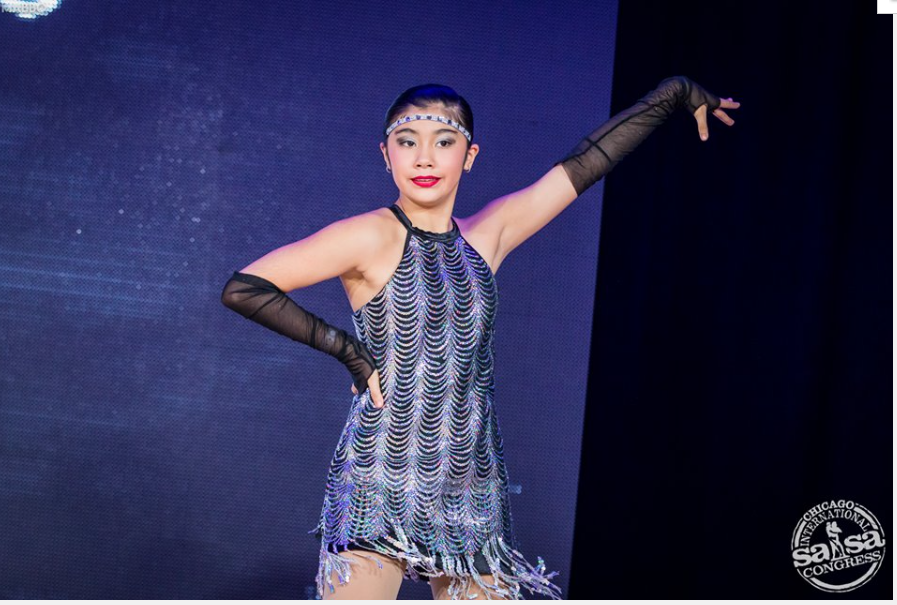 A woman in a dress and black gloves is dancing on a stage.