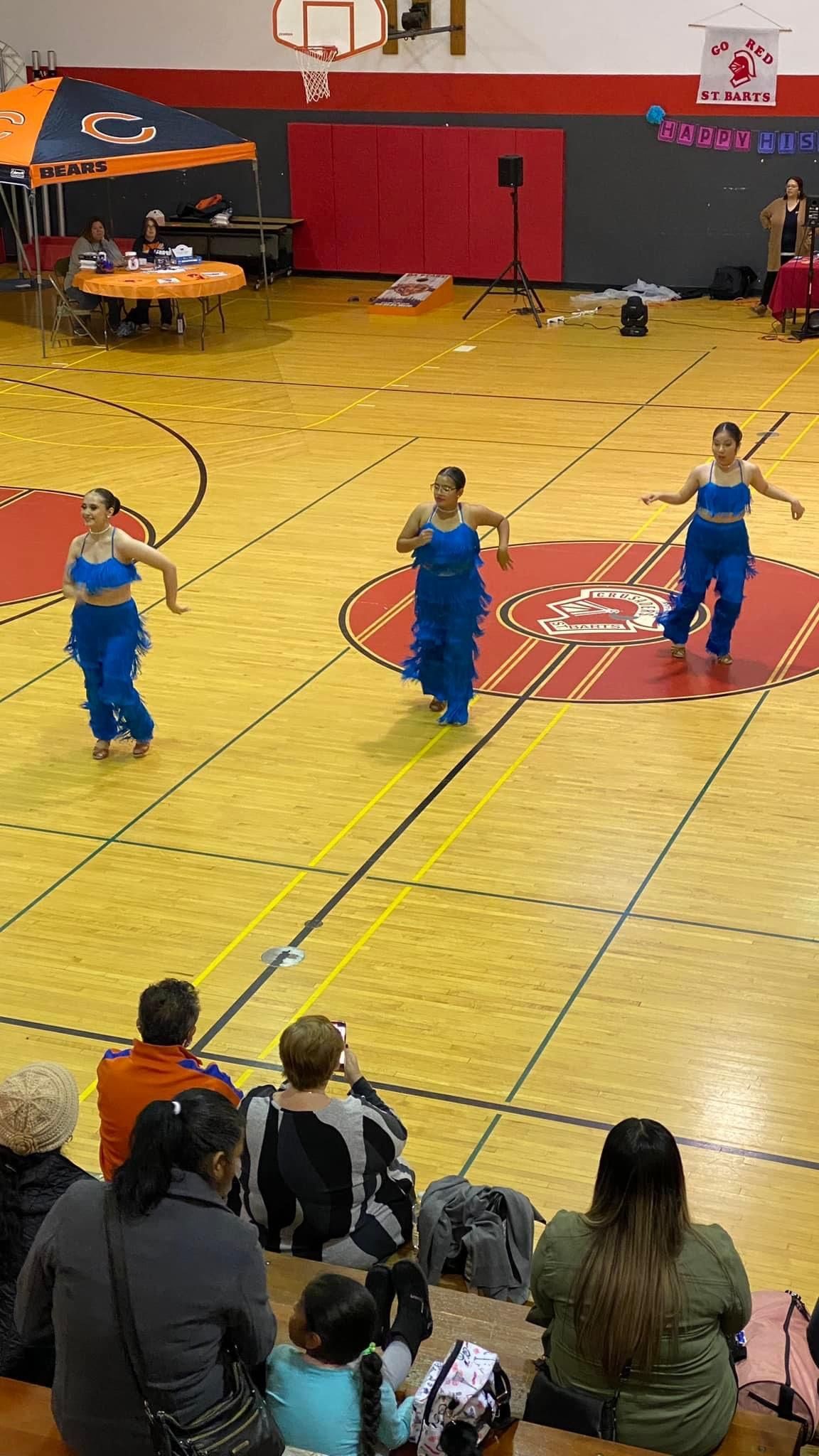 A group of people are watching a dance performance on a basketball court.