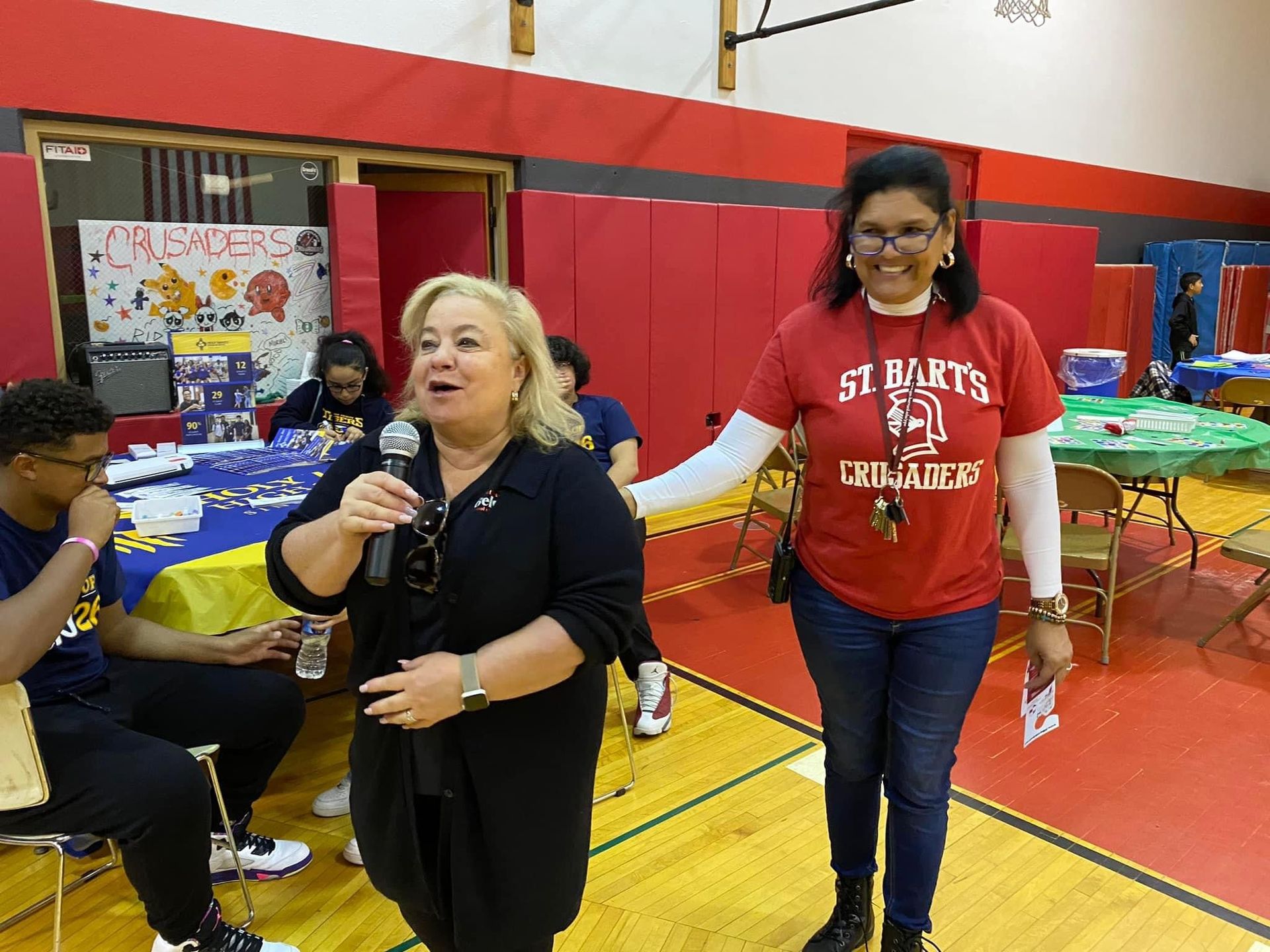 Two women are standing in a gym talking into microphones.
