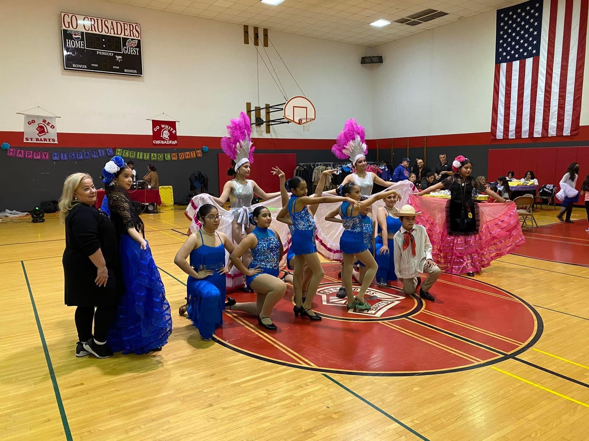 A group of people are dancing on a basketball court in a gym.
