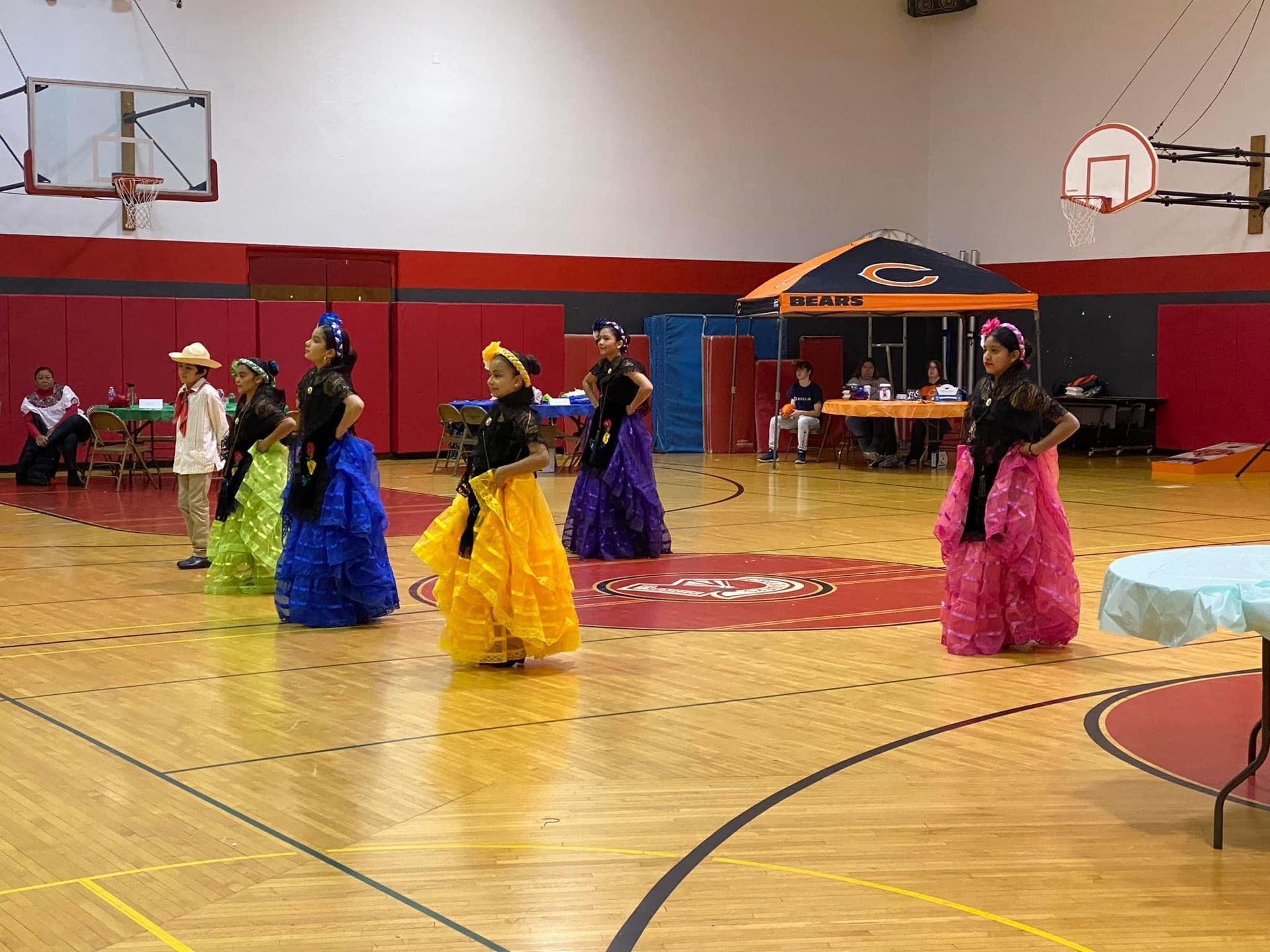 A group of women in colorful dresses are dancing on a basketball court.