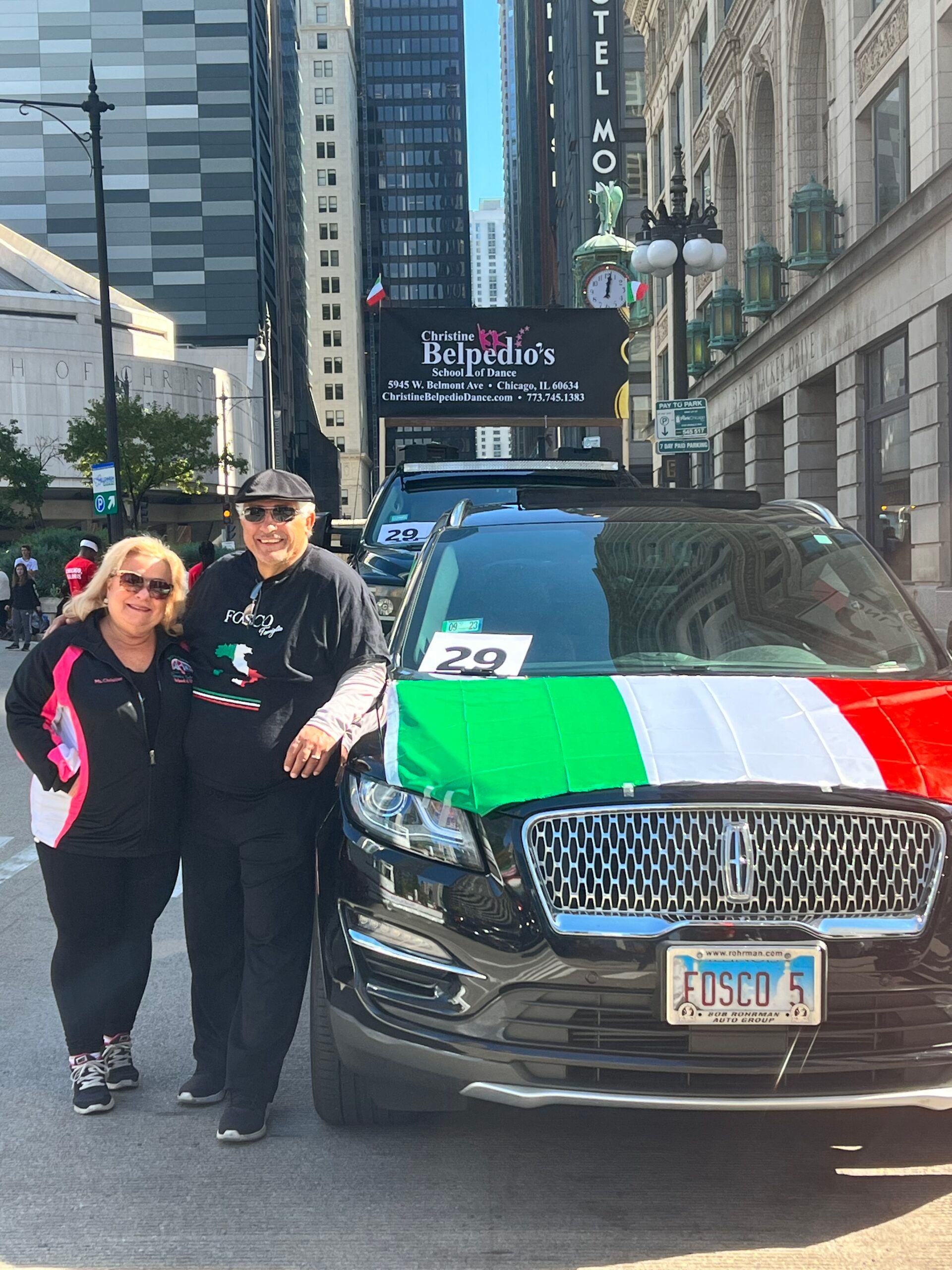 A man and a woman are standing in front of a car with a flag on it.