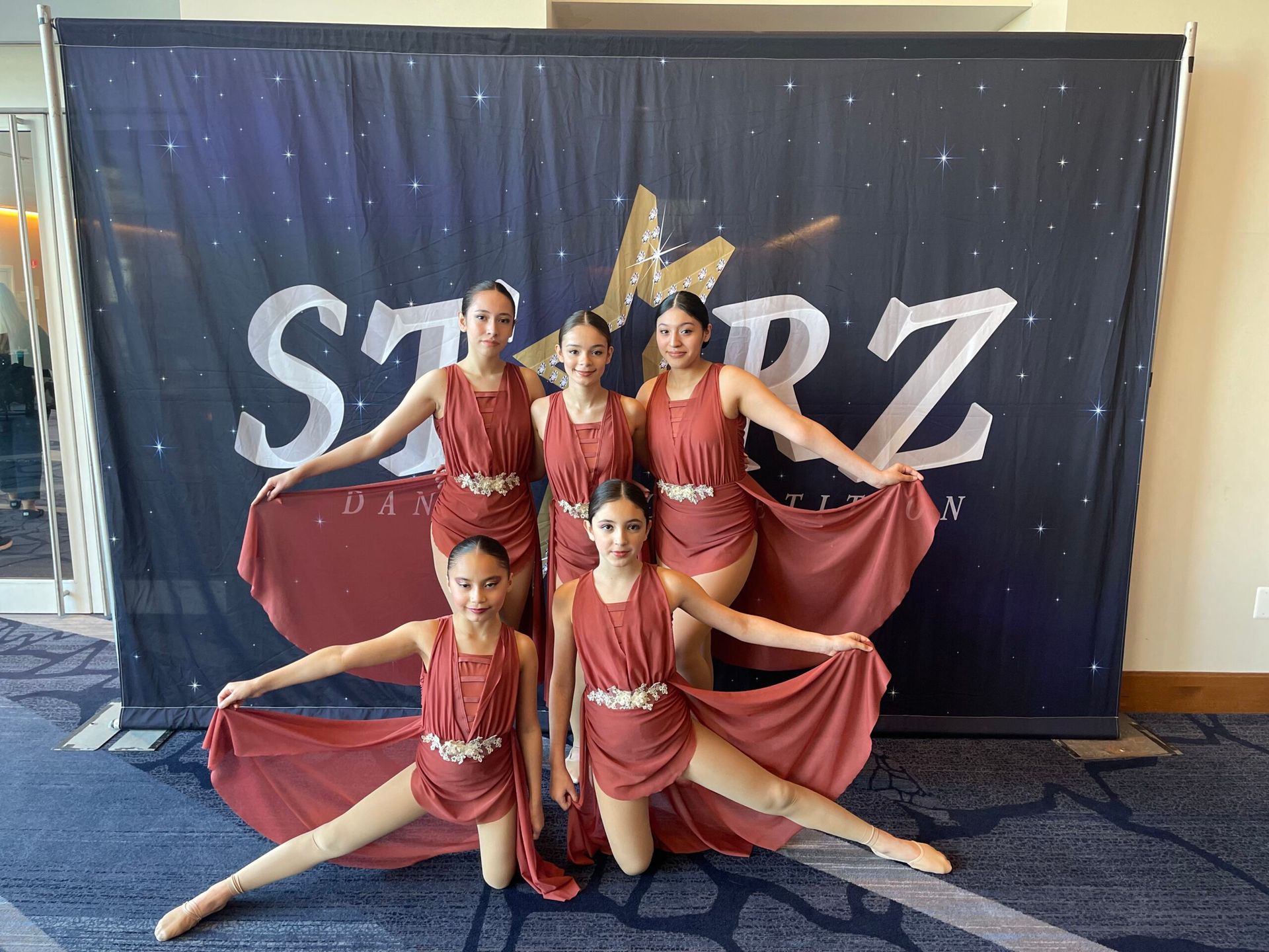 A group of young girls are posing for a picture in front of a starz banner.