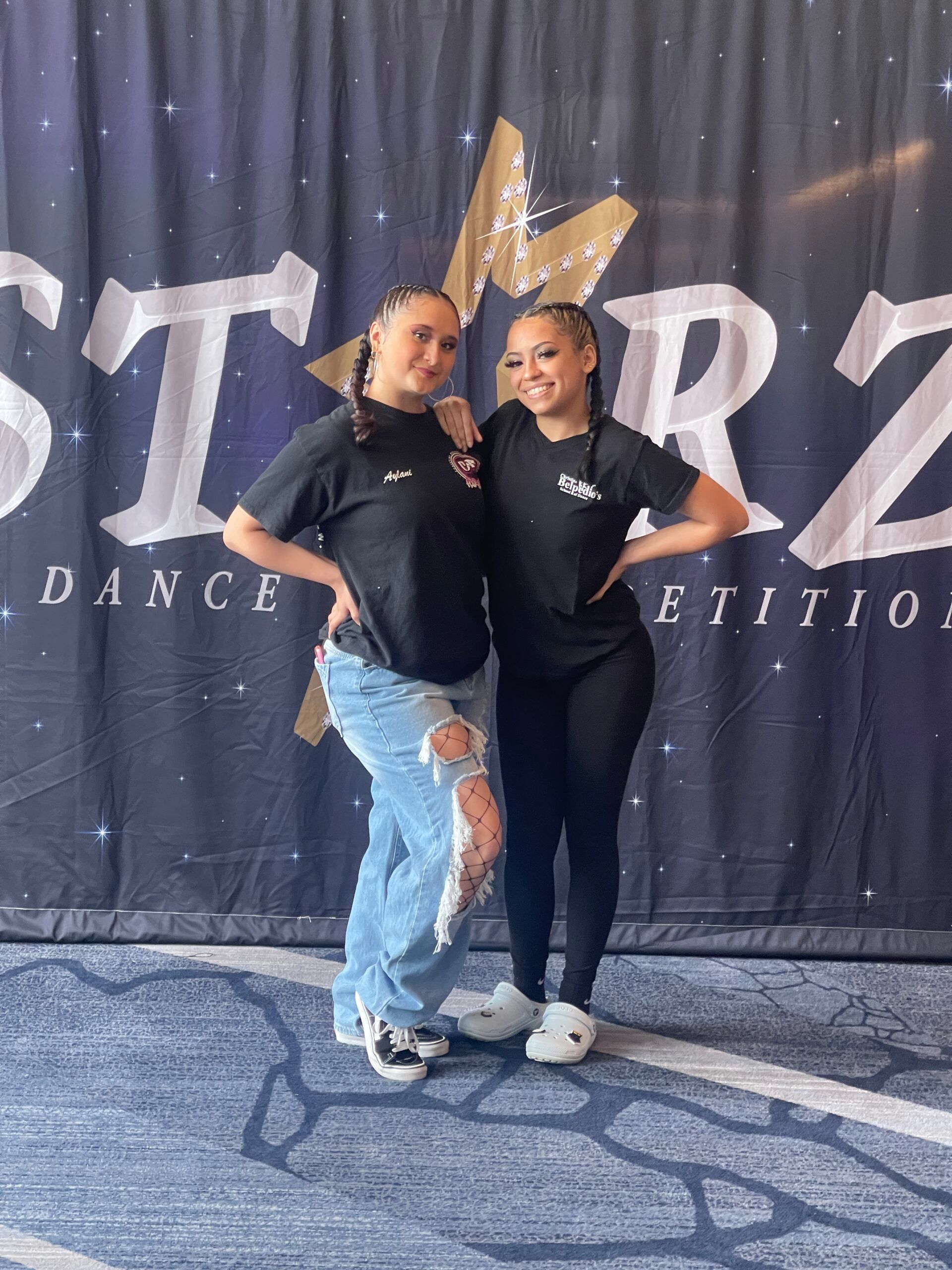 Two women are standing next to each other in front of a starz dance competition banner.