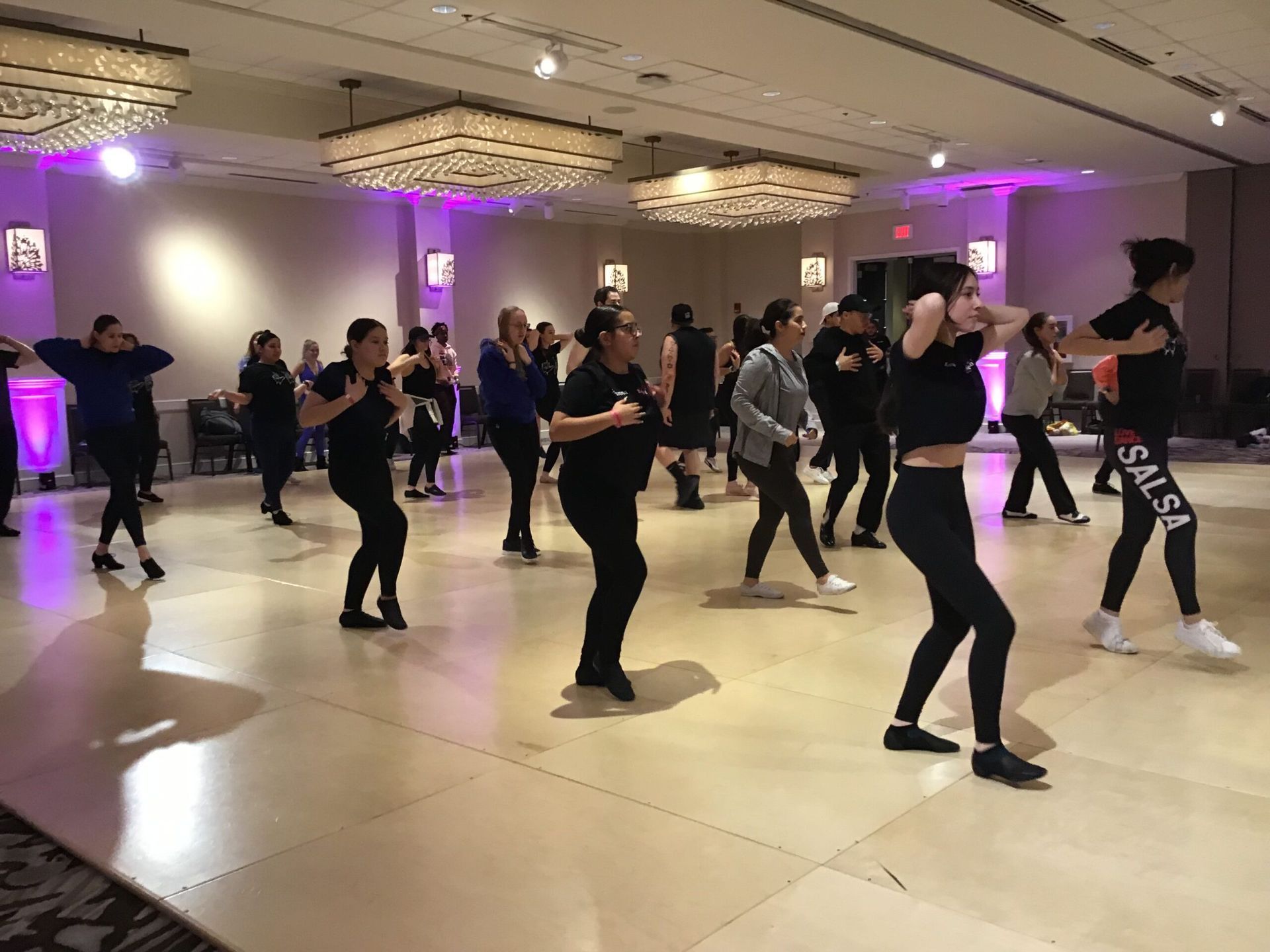 A group of people are dancing on a dance floor in a large room.