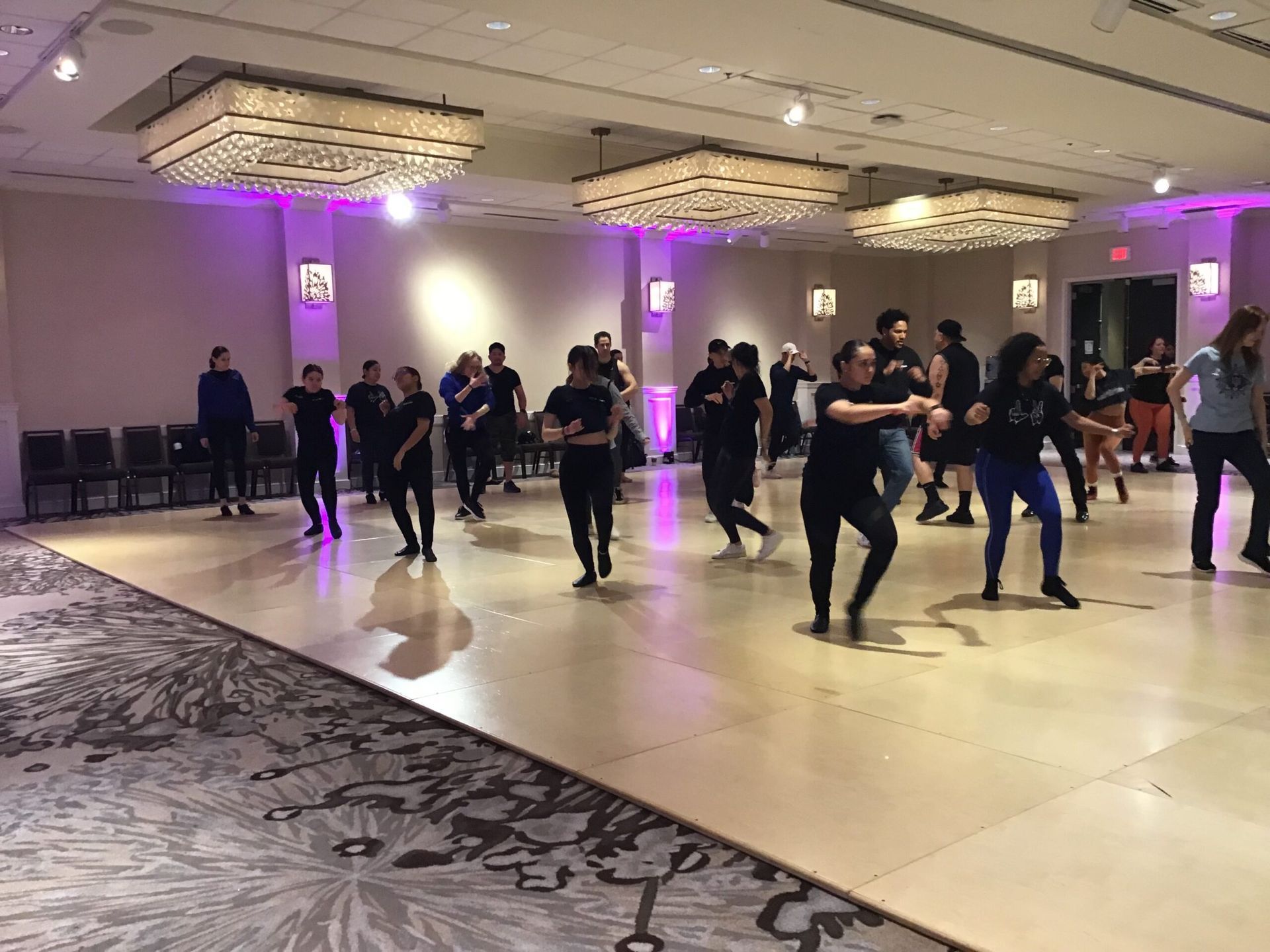 A group of people are dancing on a dance floor in a large room.