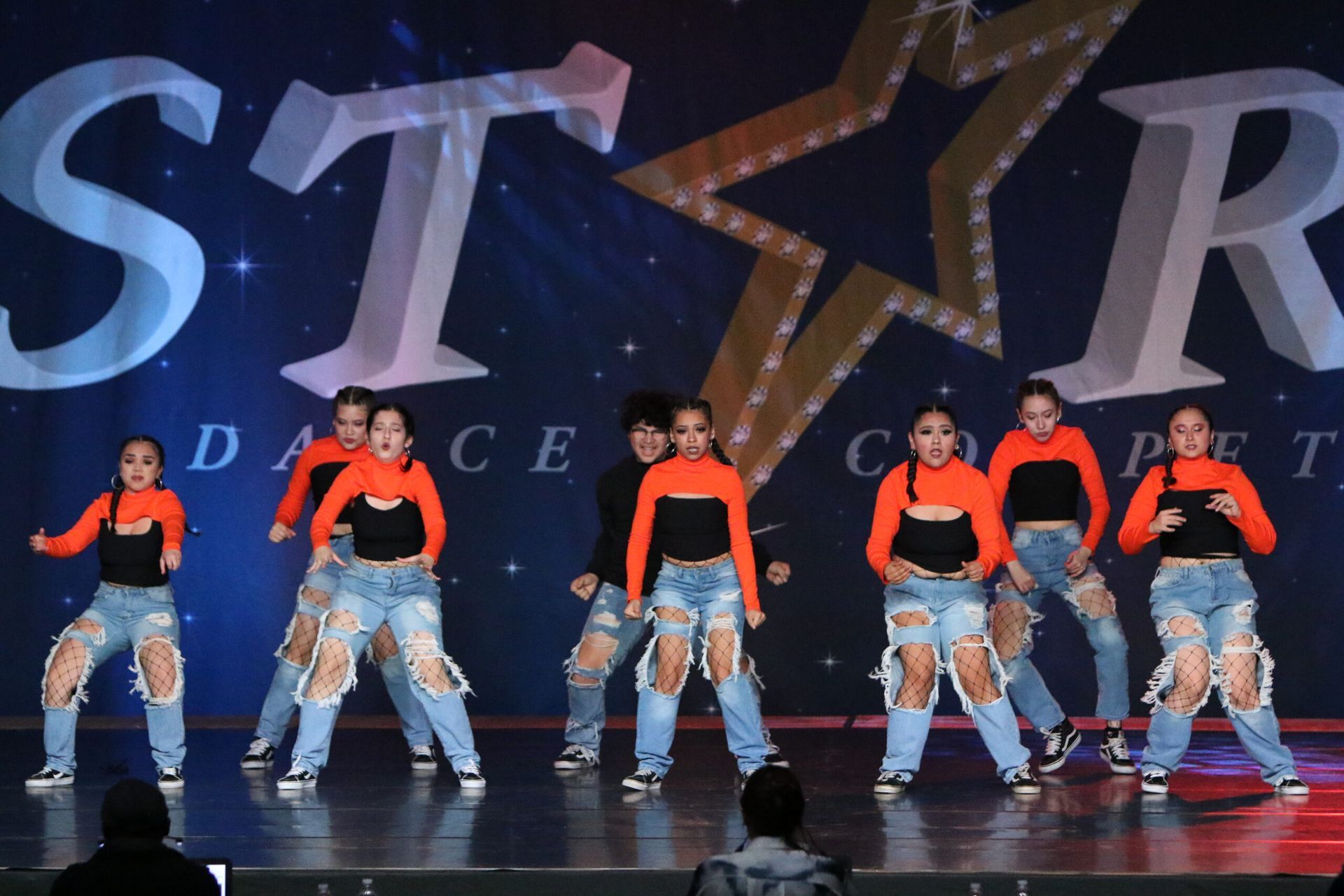 A group of young girls are performing on a stage in front of a star logo