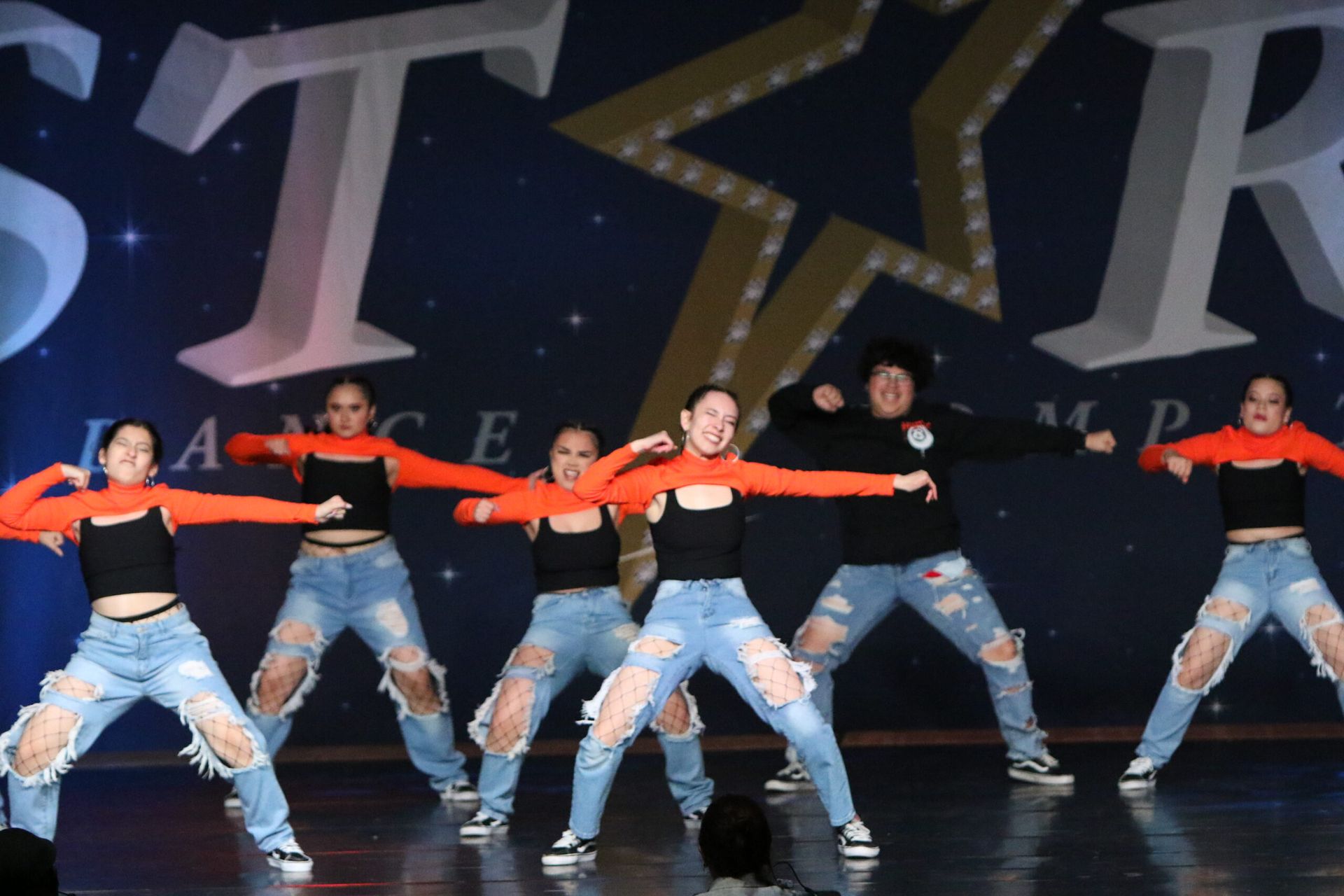 A group of young women are dancing on a stage in front of a sign that says star