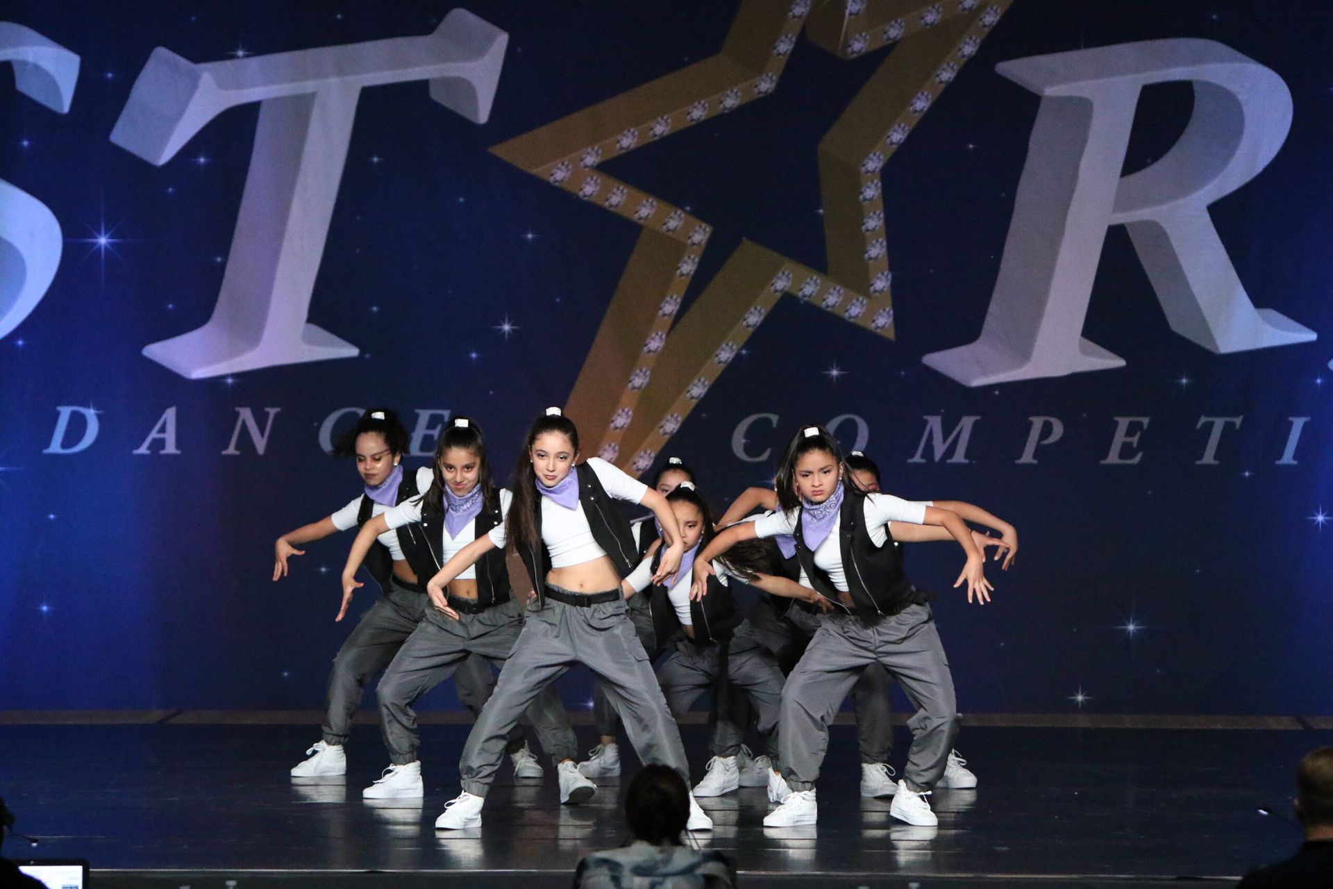 A group of young girls are dancing on a stage in front of a star dance competition sign.