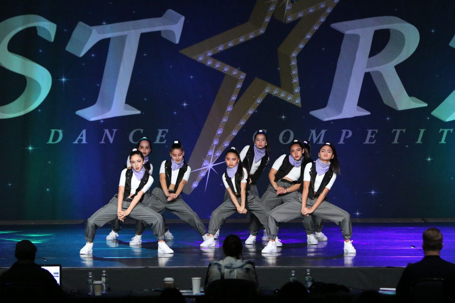 A group of young girls are dancing on a stage in front of a star dance competition logo.