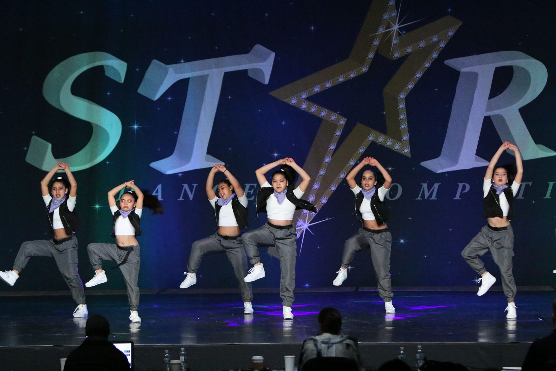A group of young women are dancing on a stage in front of a star logo.