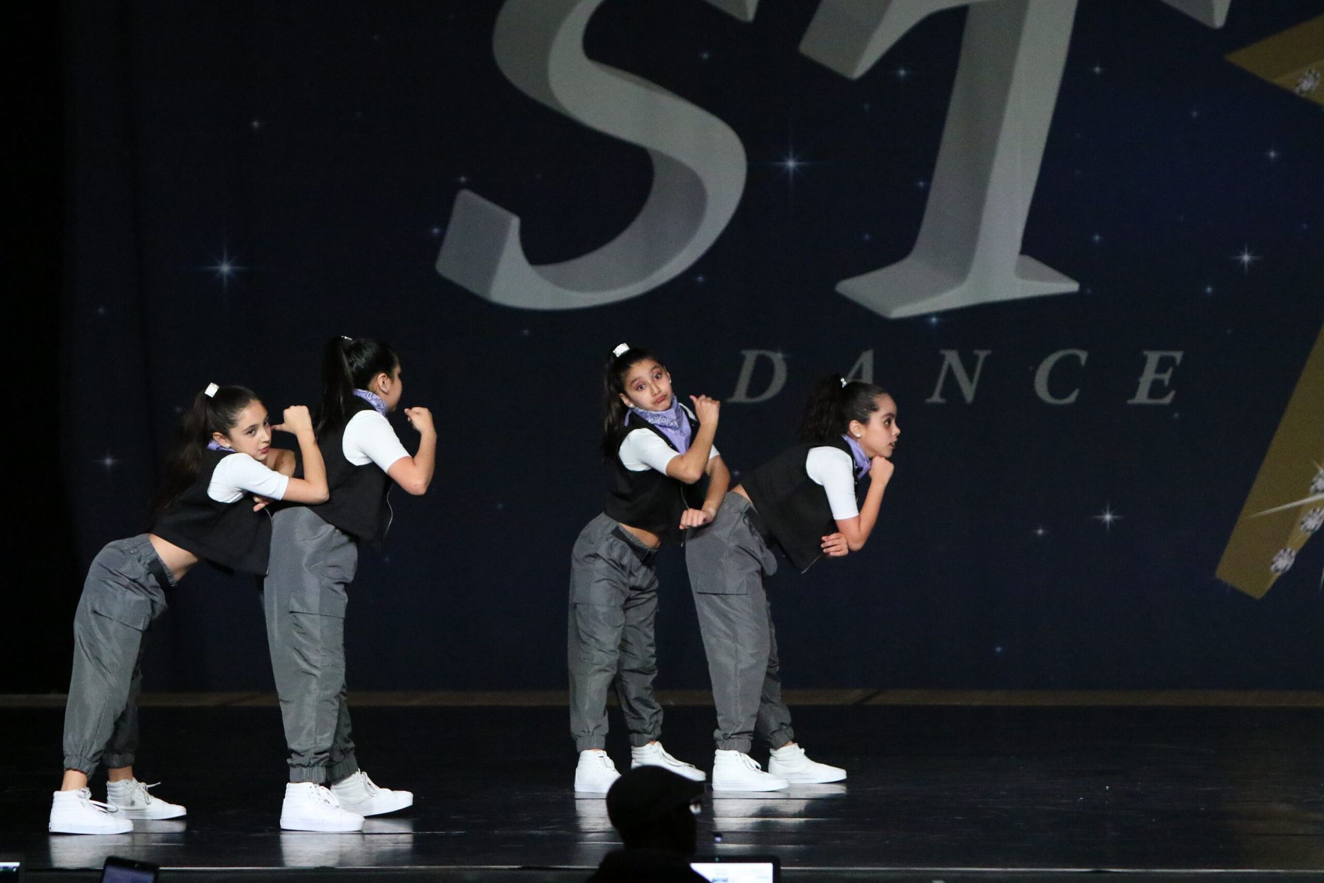 A group of young girls are performing on a stage in front of a sign that says dance.