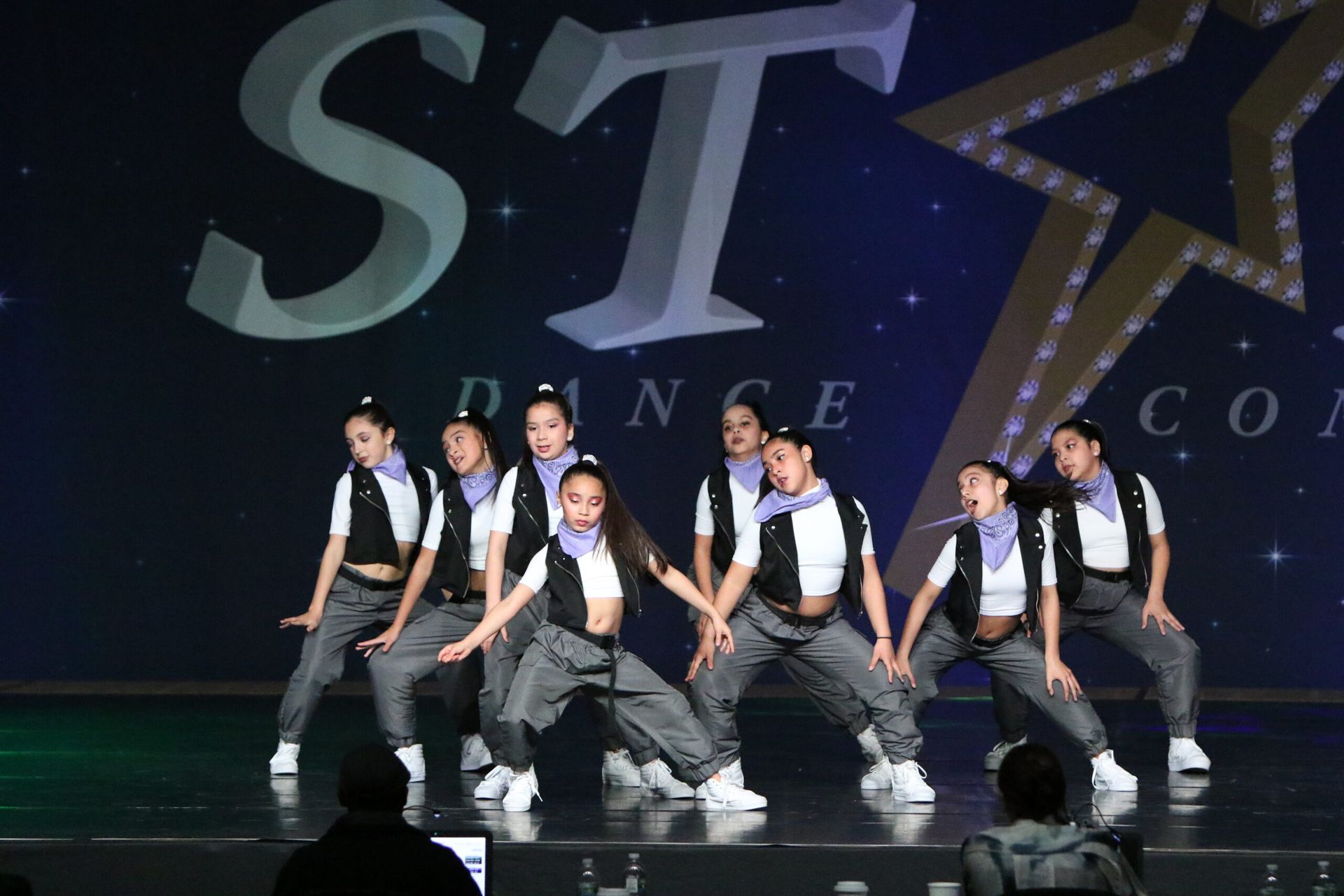 A group of young girls are dancing on a stage in front of a star.