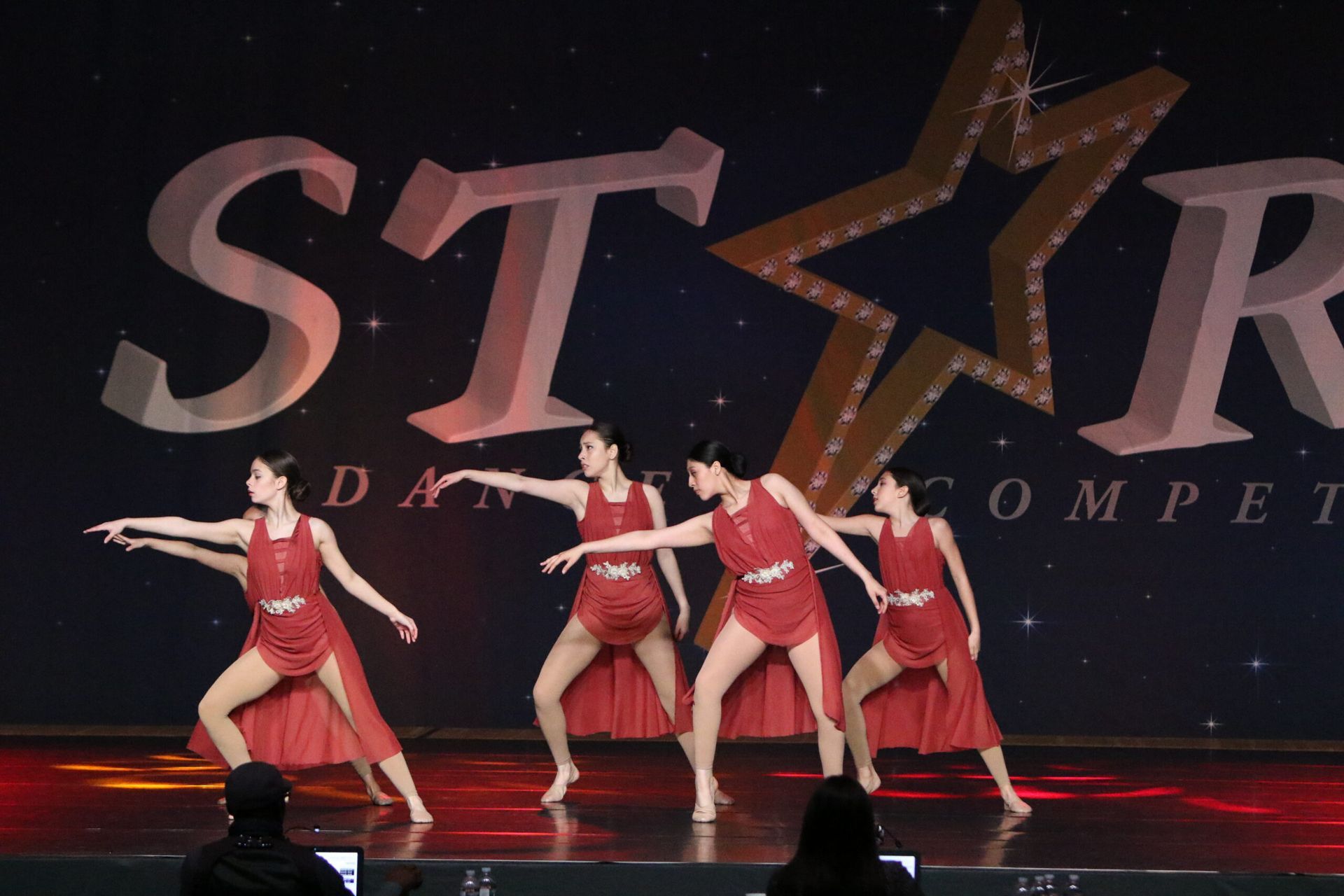 A group of women are dancing on a stage in front of a star logo