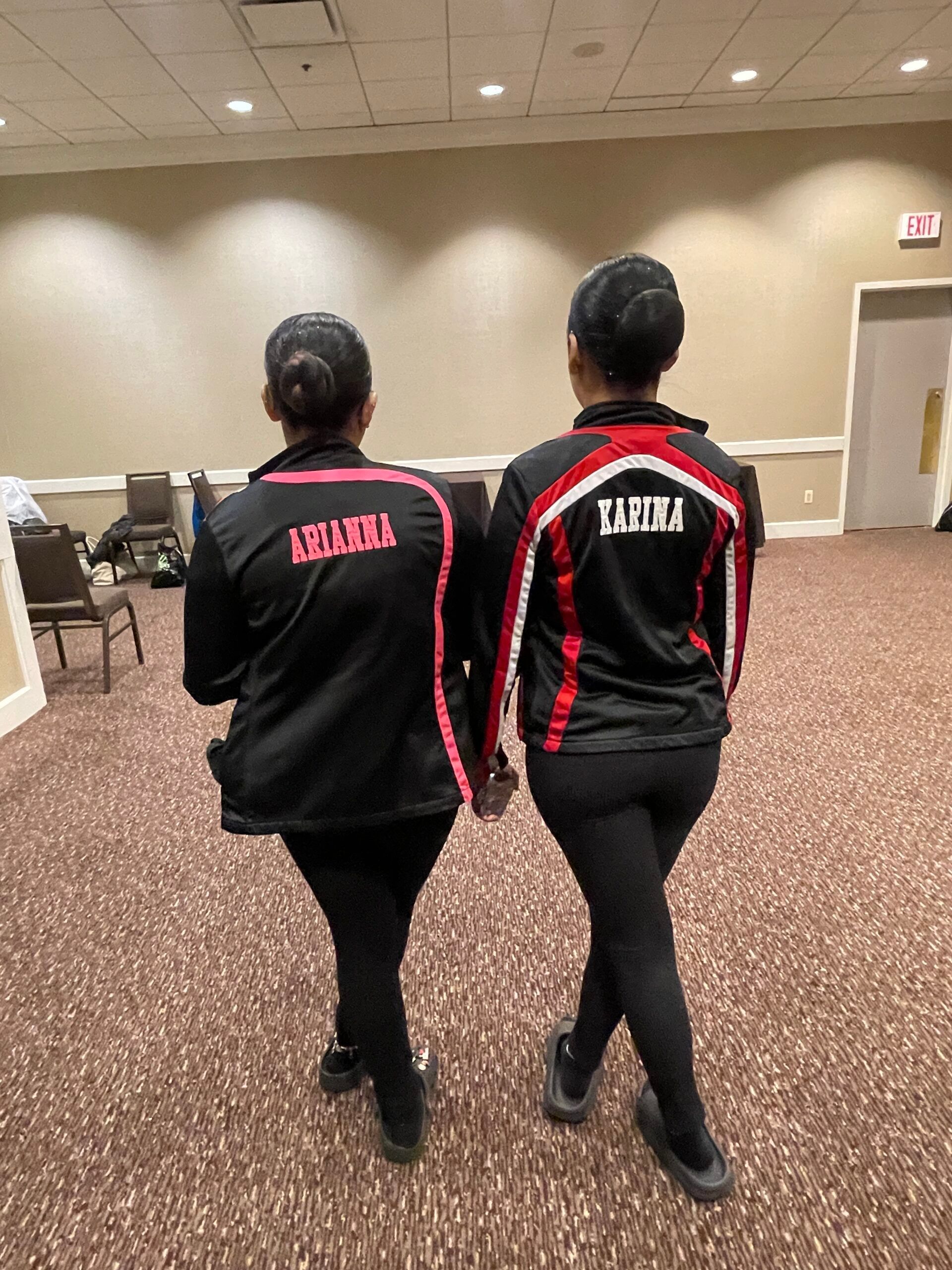 Two women are standing back to back in a room holding hands.