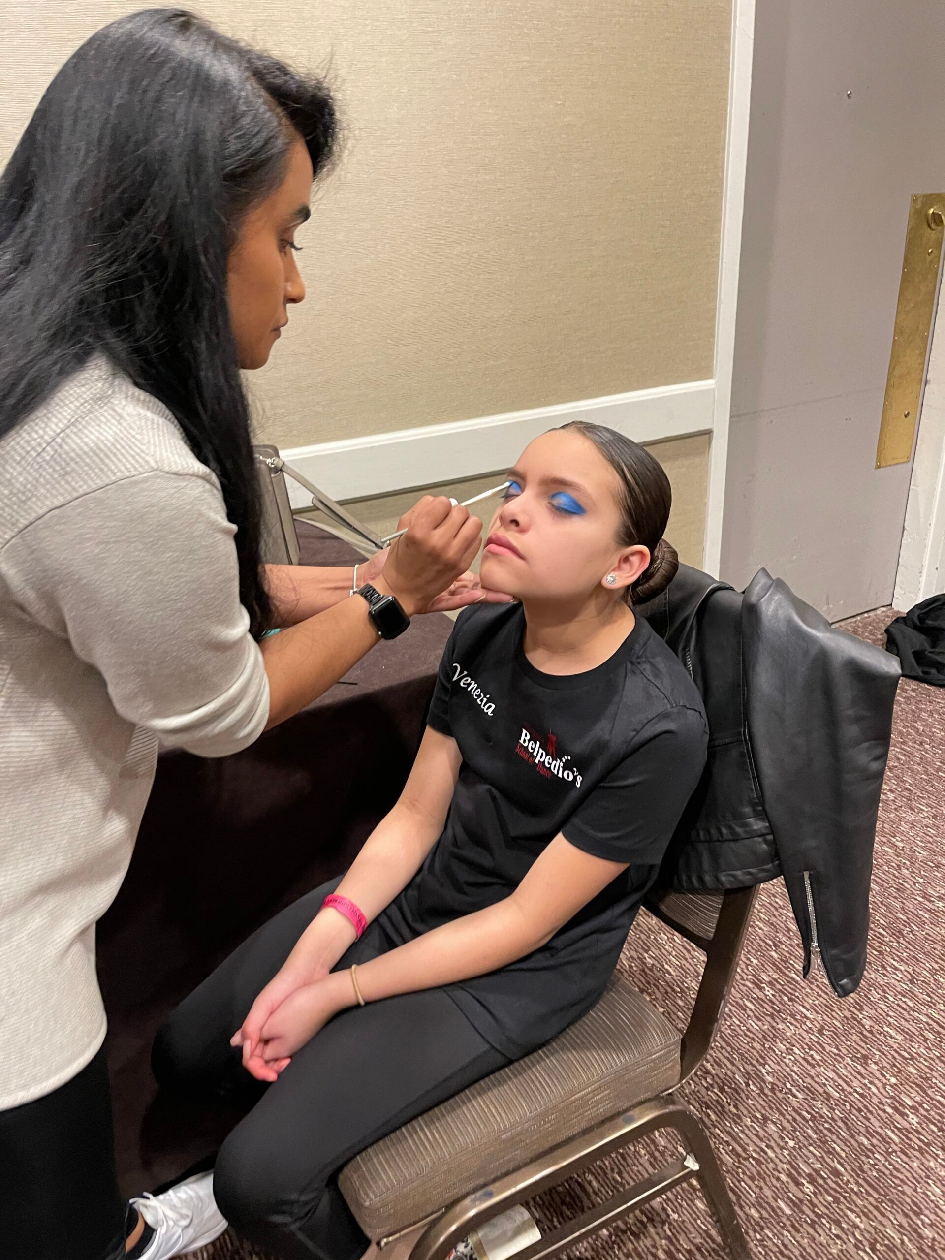 A woman is applying makeup to a girl who is sitting in a chair