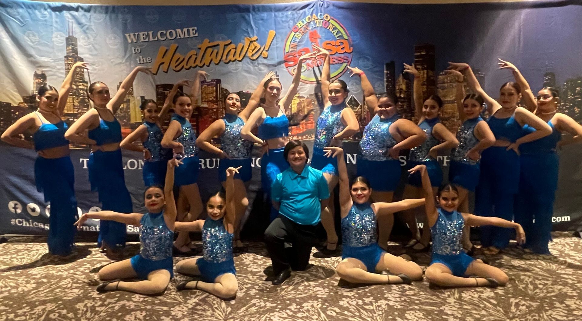 A group of dancers are posing for a picture in front of a sign that says welcome.