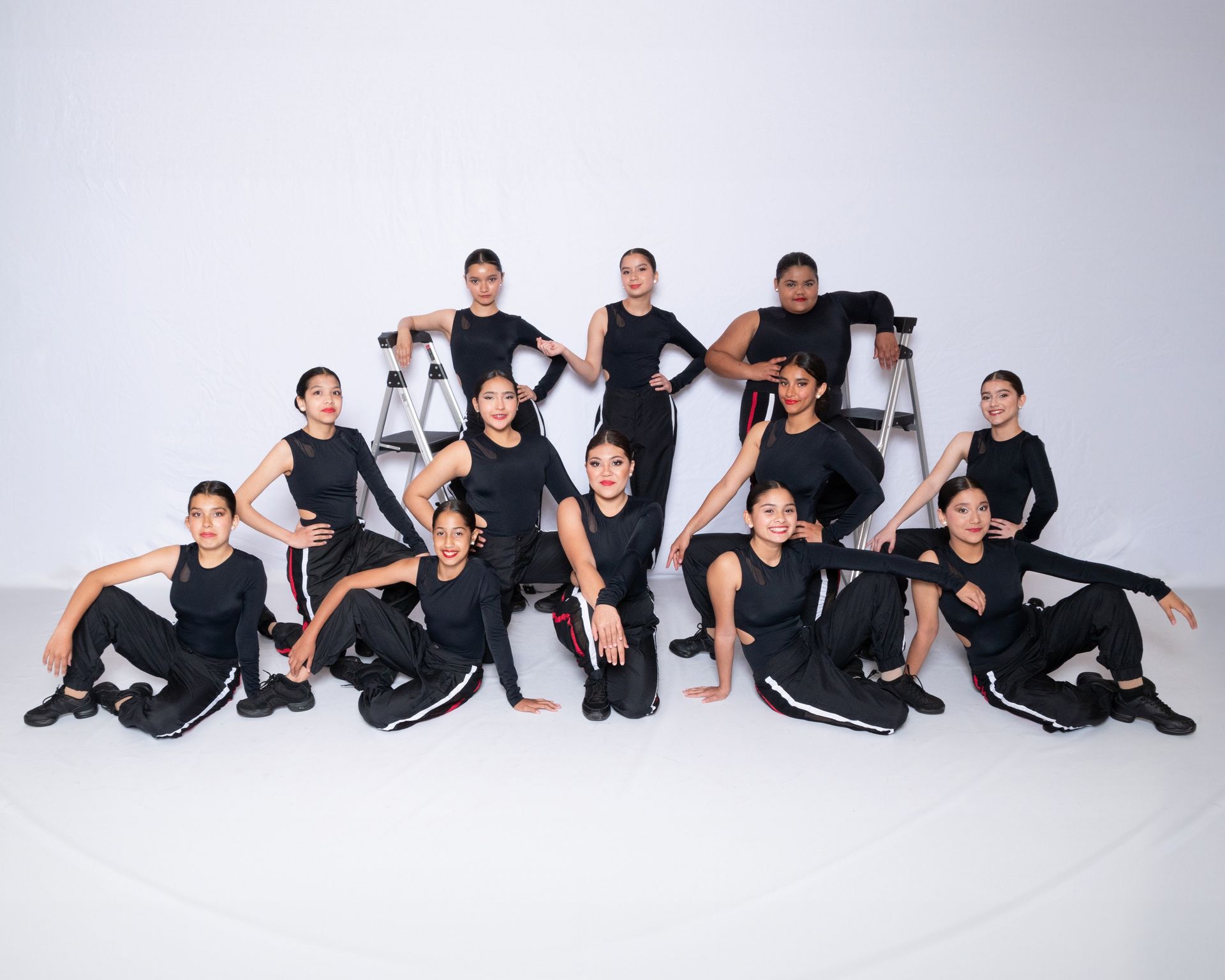 A group of young dancers are posing for a picture in front of a white wall.