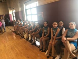 A group of young girls are sitting on a bench in a gym.