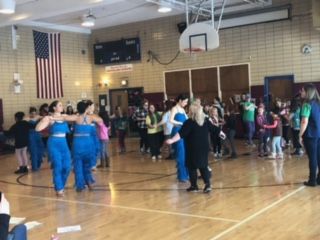 A group of people are dancing in a gym.