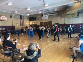 A woman is taking a picture of a group of people dancing in a gym.
