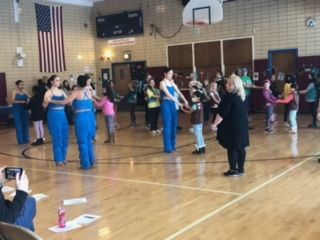 A group of people are dancing in a gym in front of an american flag.