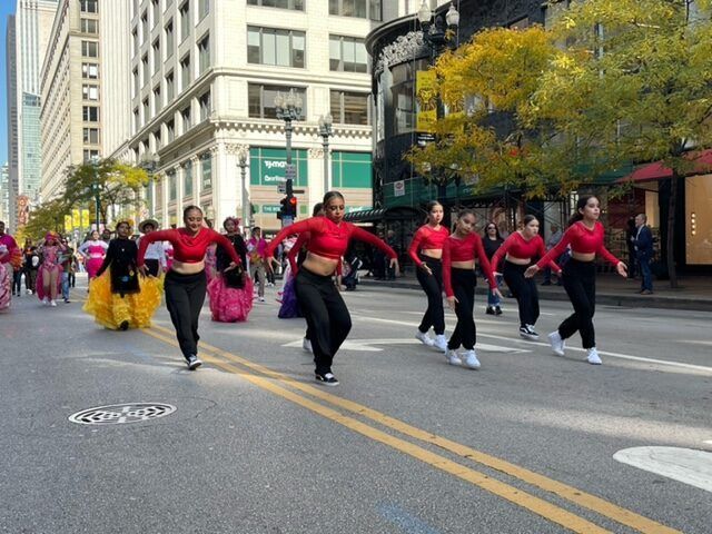 A group of women are dancing in a parade down a city street.
