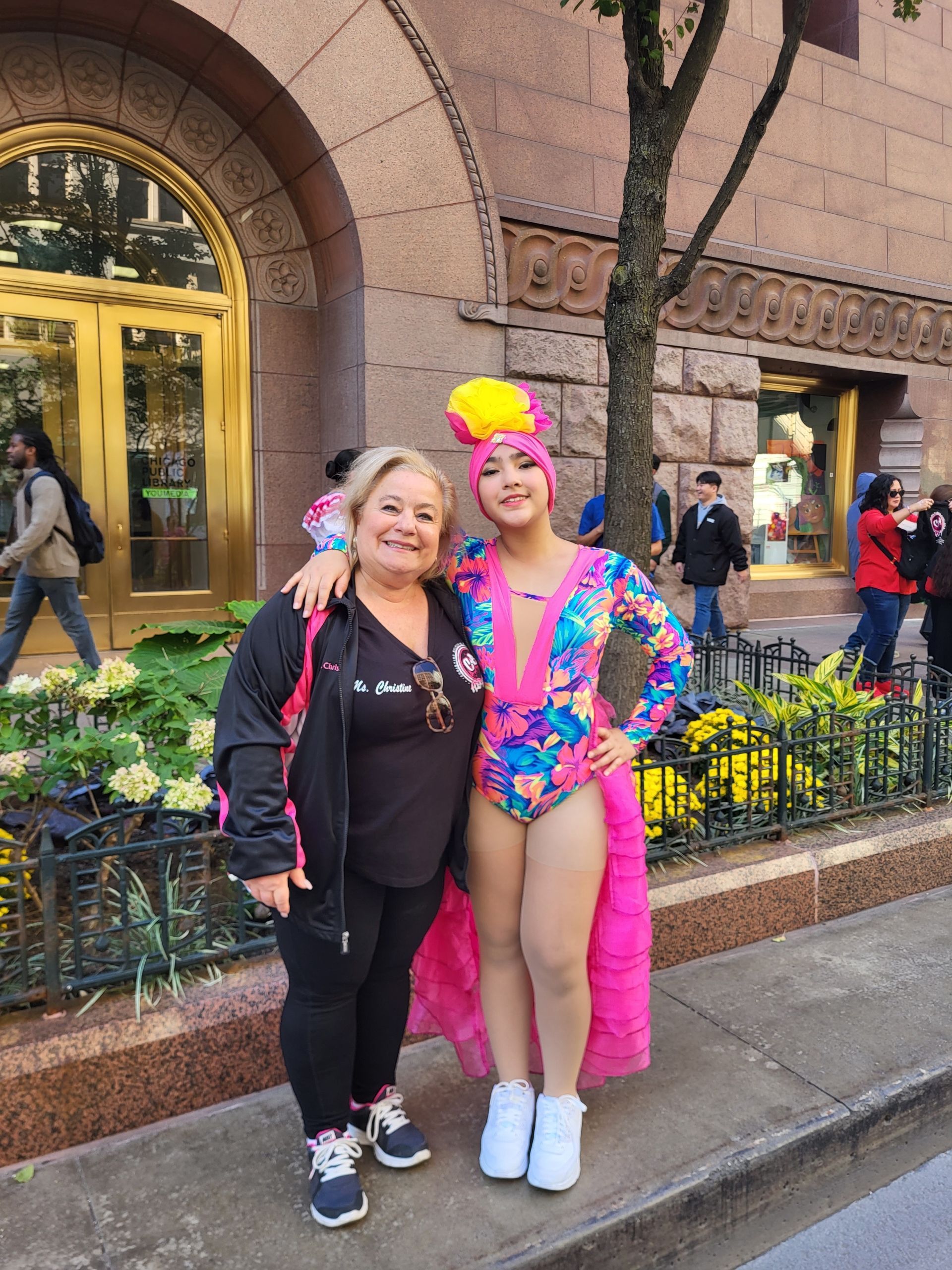 Two women are standing next to each other on a sidewalk in front of a building.