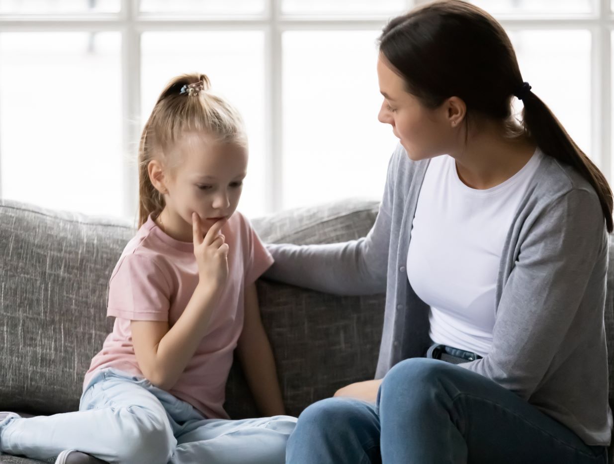 Woman comforts a child on a couch; the child looks sad while the woman has a gentle expression.