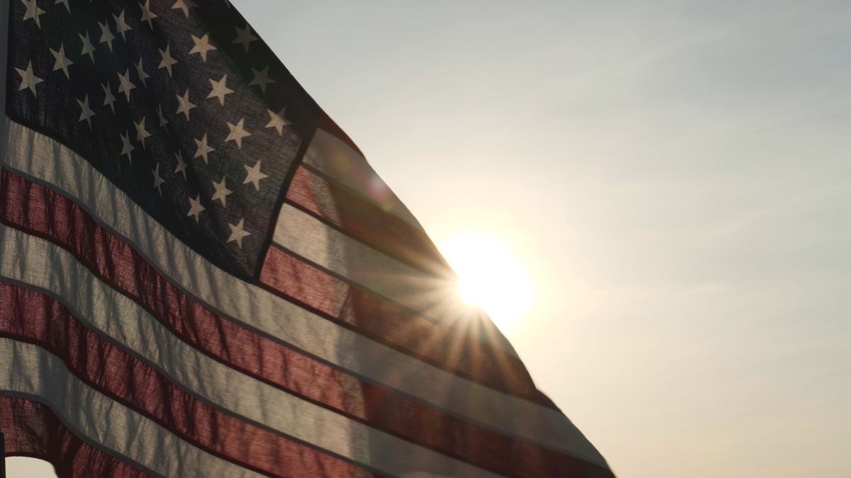 American flag waving in the sunlight with the sun peaking through.