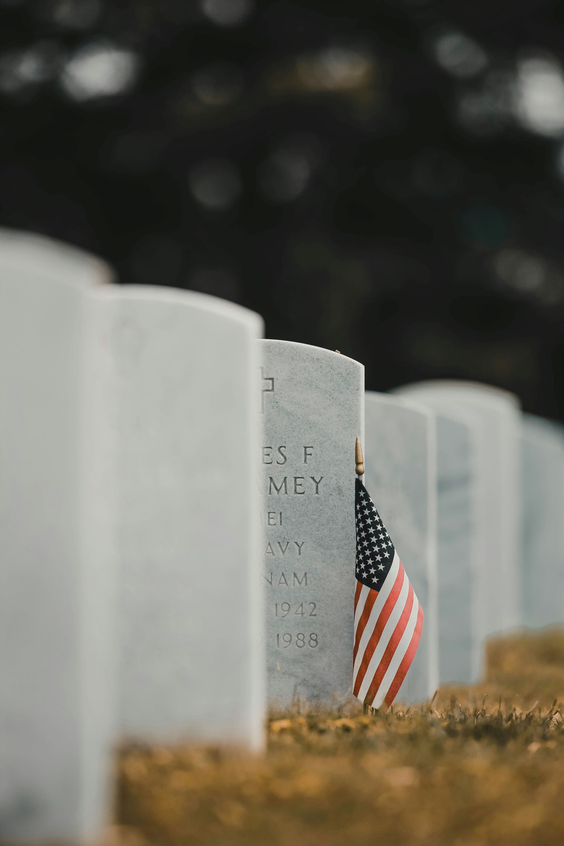 Row of white headstones in a cemetery; American flag placed in front of one.