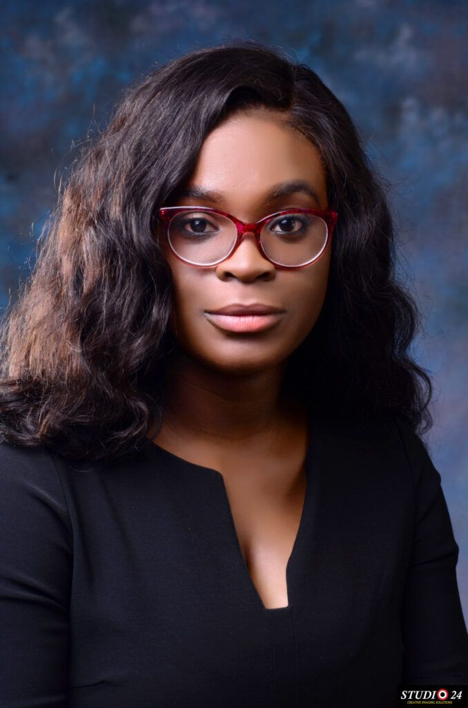A woman in a black jacket and pearl necklace is smiling for the camera.
