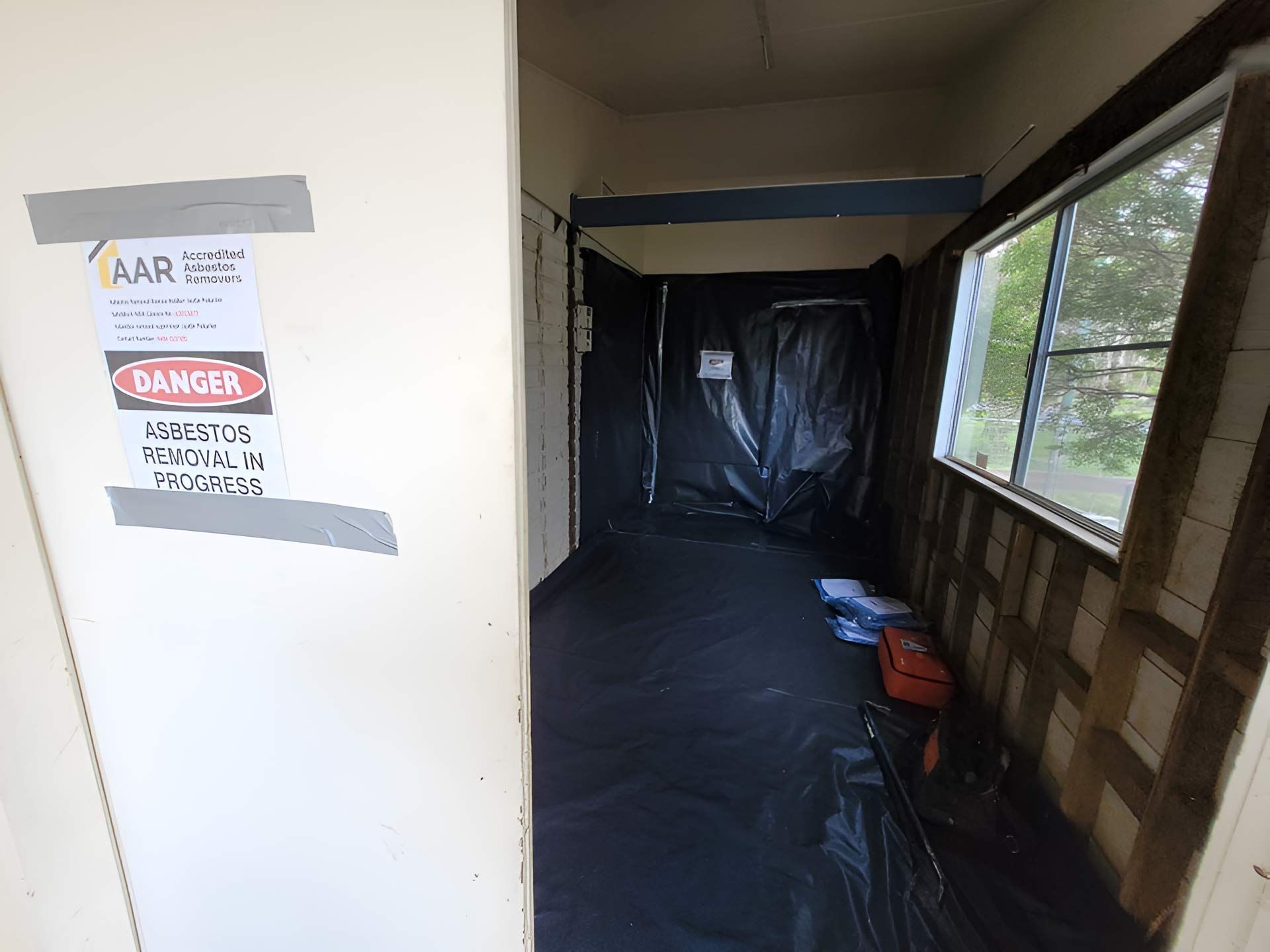 A Hallway With A Asbestos Danger Sign Taped To The Wall — Accredited Asbestos Removers in Casino, NSW