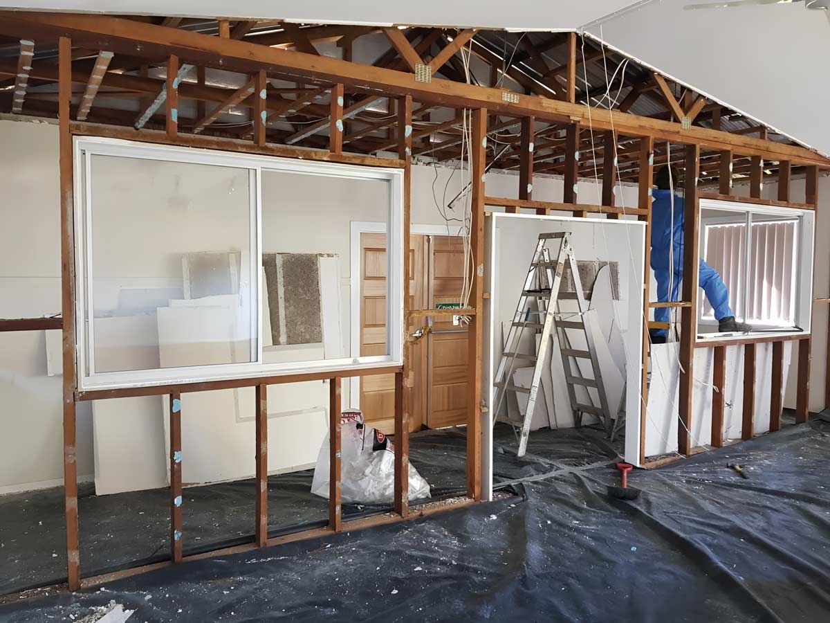A Man Is Standing On A Ladder In A Room That Is Being Remodeled — Accredited Asbestos Removers in Lismore, NSW