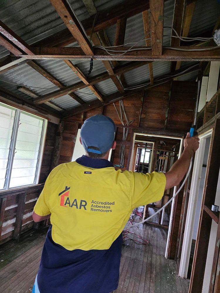 Person in Yellow Shirt Spraying Inside a Gutted Building — Accredited Asbestos Removers in Lismore, NSW