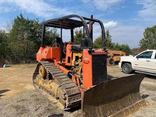 A bulldozer is parked in a gravel lot next to a white truck.