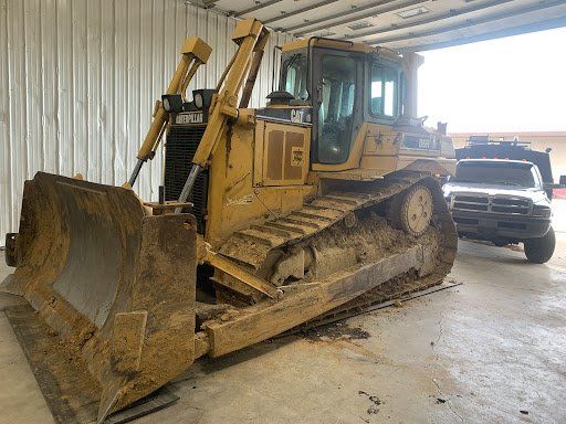 A bulldozer is parked in a garage next to a truck.