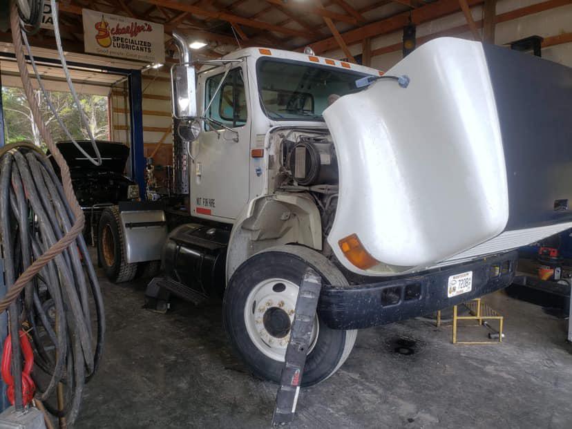 A white truck is sitting in a garage with its hood up.