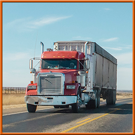 A red semi truck is driving down a highway.
