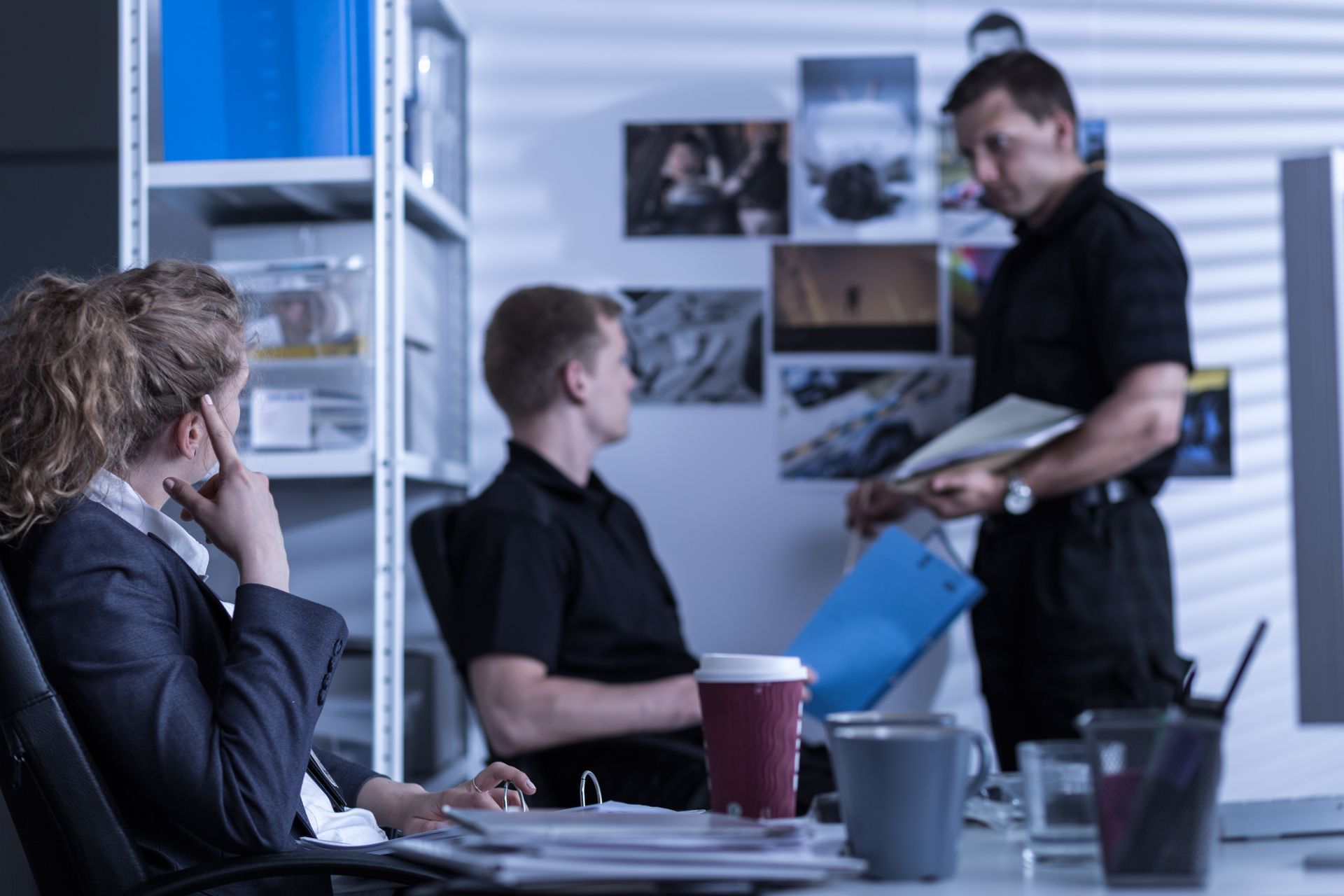 Police officers in office, discussing a case. One holds documents, others listen, reviewing evidence.