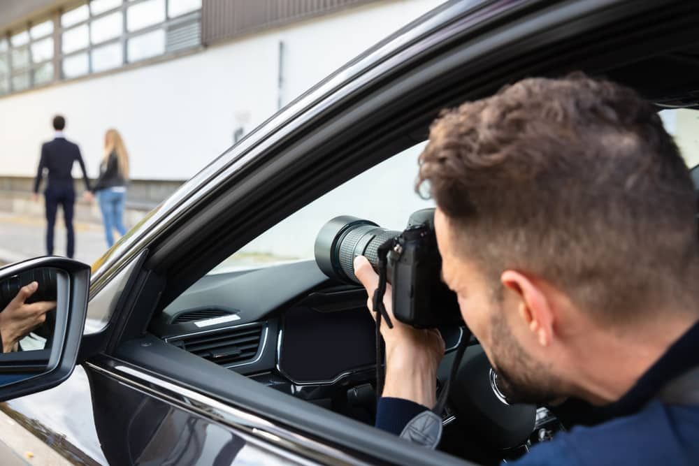 Private investigator taking surveillance photos from a vehicle as a couple walks away