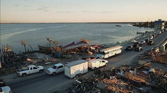 A row of cars are driving down a road next to a body of water.