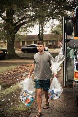 A man is carrying bags of toilet paper and bottles to a bus.