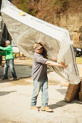 A man is carrying a large mattress wrapped in plastic.