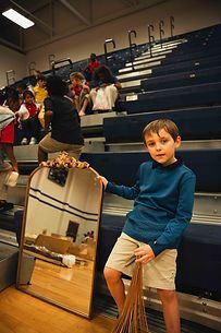 A young boy is holding a mirror and a broom in a gym.