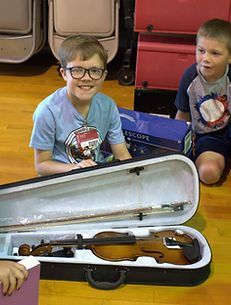 A young boy is sitting next to a violin in a case.