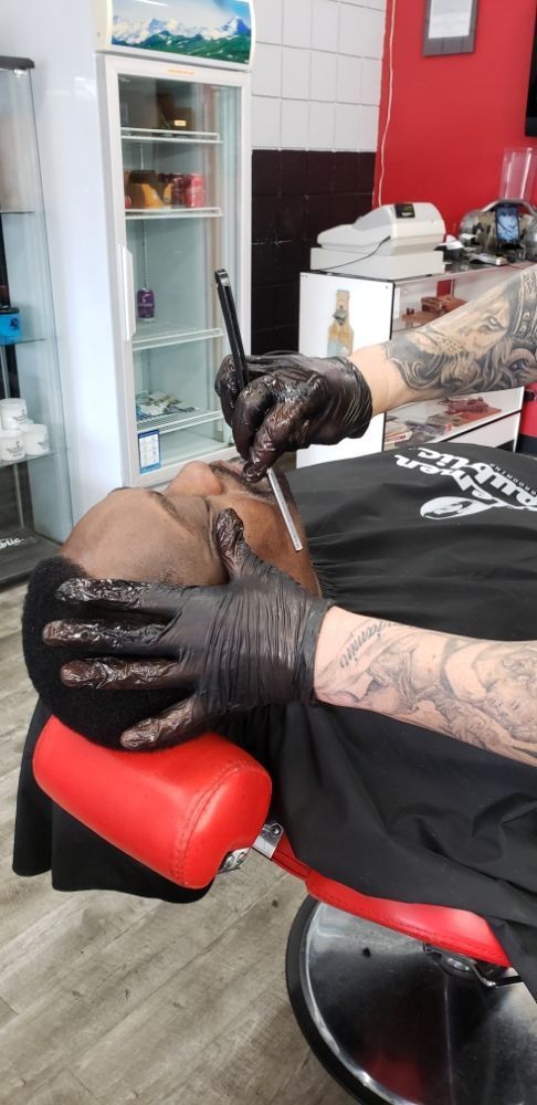 A man is getting a tattoo on his leg in a barber shop.