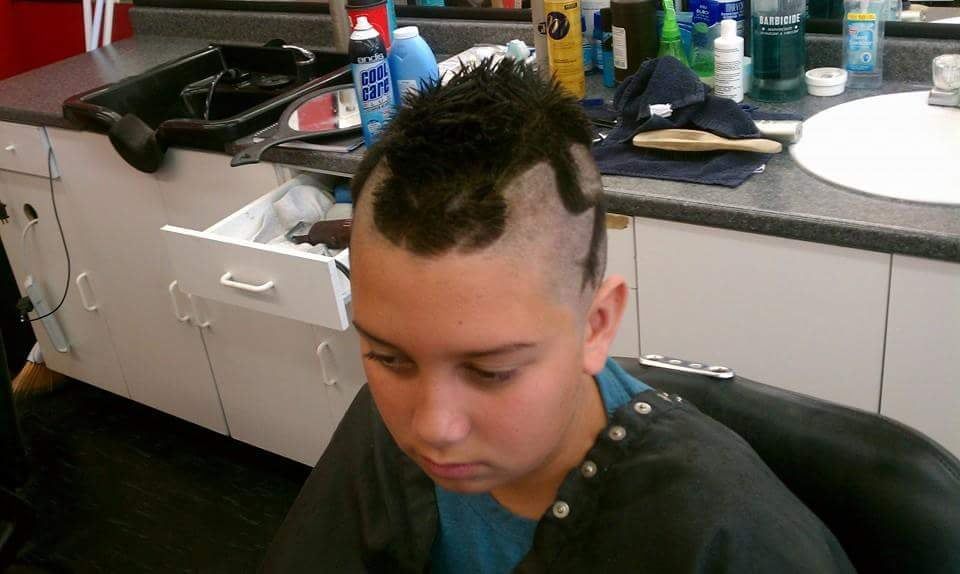 A young boy is getting his hair cut at a barber shop.