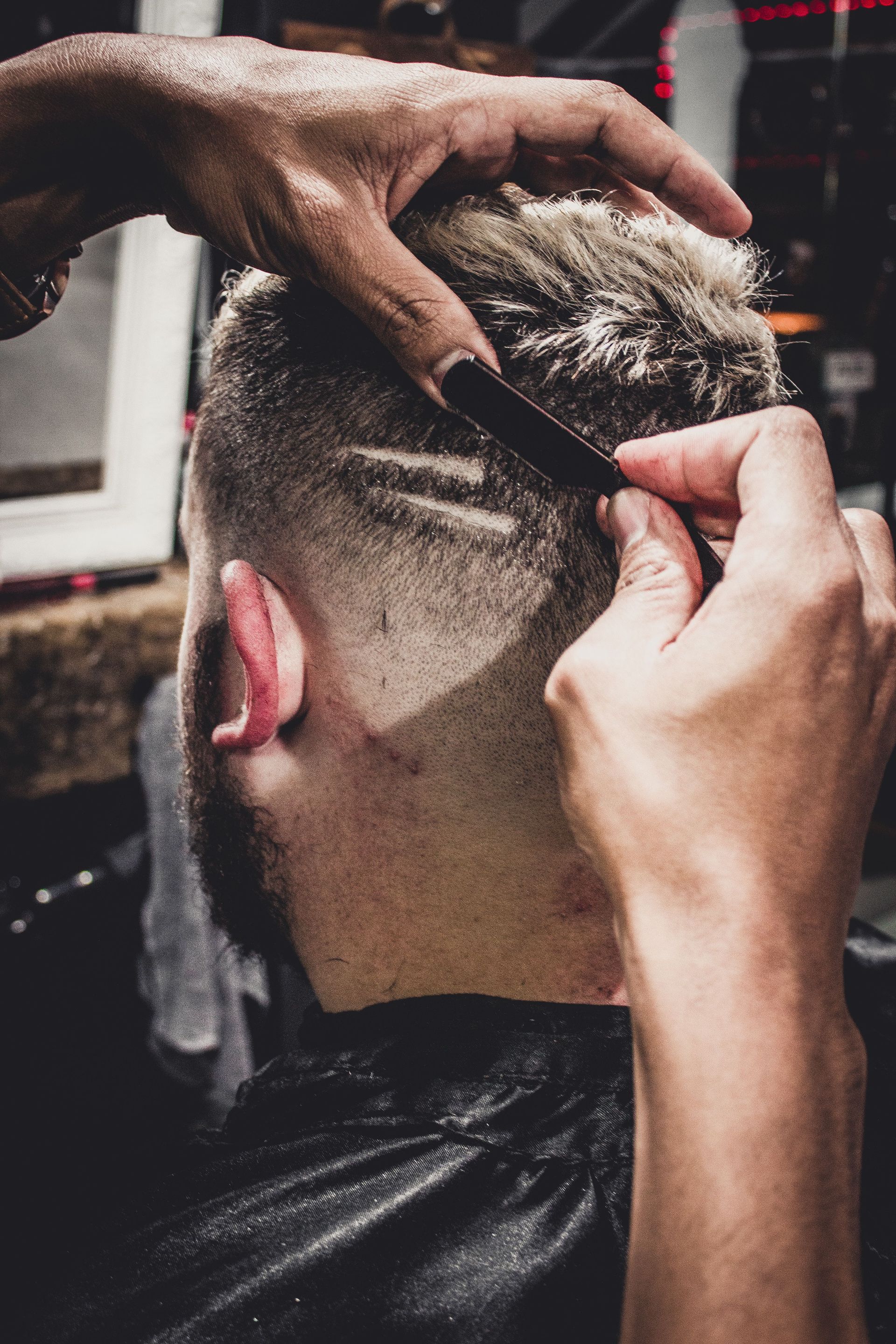 Haircut in progress, barber trimming a fade with clippers on the back of a client’s head