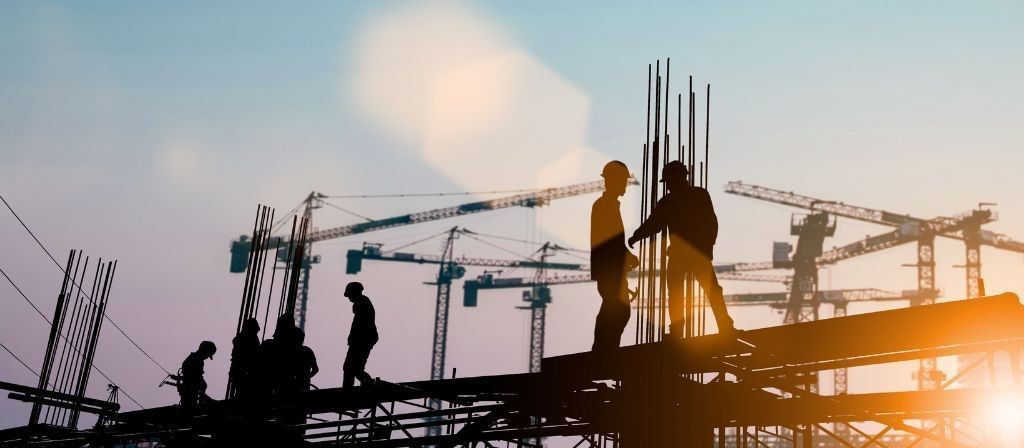 Silhouettes d'ouvriers du bâtiment sur un chantier avec des grues en arrière-plan au coucher du soleil.